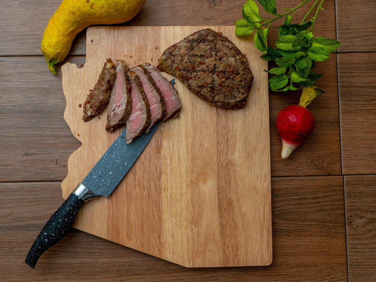 Arizona-shaped cutting board holding sliced steak and vegetables.