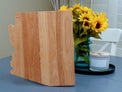 Arizona-shaped cutting board displayed upright beside flowers.