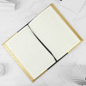 Gold journal notebook open to lined pages on a marble surface.