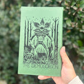 Green engraved journal held outdoors to show a detailed cover design.